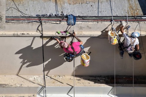 Painter hanging from a rope while working on a façade, symbolic image for safety in construction,