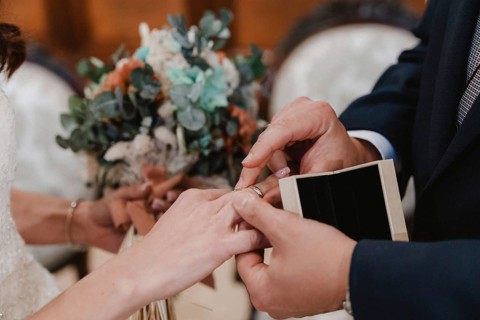Close up of a couple exchanging rings during a wedding ceremony, with a beautiful bouquet in the