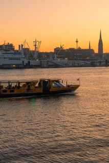 A ship on a river at sunset with the city silhouette in the background, Hamburg, Germany