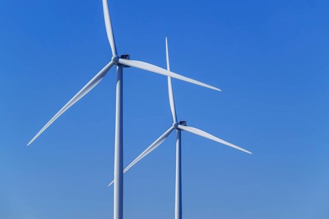 Two wind turbines showing tower, nacelle and huge rotor blades against blue sky