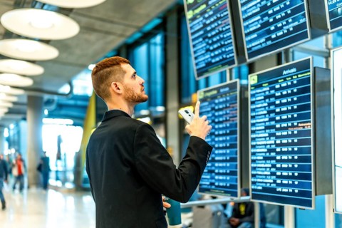 Businessman holding smartphone and pointing at timetable display, checking flight information in