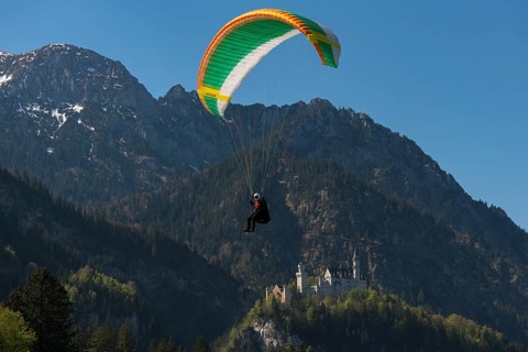 A paraglider flies near Neuschwanstein Castle in front of an impressive mountain landscape,