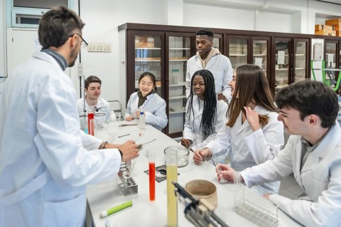 Multi ethnic university students wearing lab coats listening to their chemistry teacher explaining