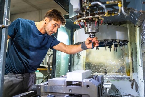 Male caucasian technician working with mechanic machine to produce plastic parts in a cnc factory