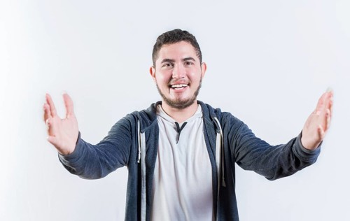Friendly young man welcoming with open arms isolated. Hospitable guy opening arms to the camera