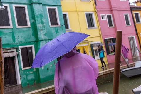 City view of Burano with colourfully painted houses and canals. Rainy weather, people are carrying