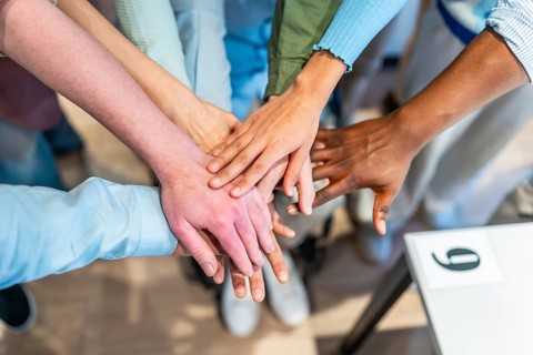 Coworkers stacking hands together, showing unity, teamwork and collaboration in the office