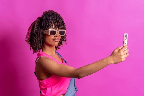 Fashionable young woman taking a selfie with smartphone, wearing sunglasses and pink top on a