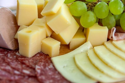 Cheese cubes and slices of sausage with grapes on a wooden board offer a classic savoury selection,