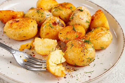 Half-eaten fried new potatoes, with butter and dill, on a white plate, with a fork, at home, no