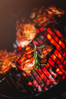 From above of delicious appetizing meat steaks with fresh rosemary grilling on rack above burning