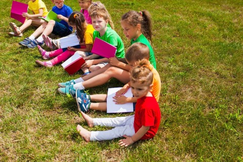The good kids in colorful t-shirts sit on the grass with books in their hands