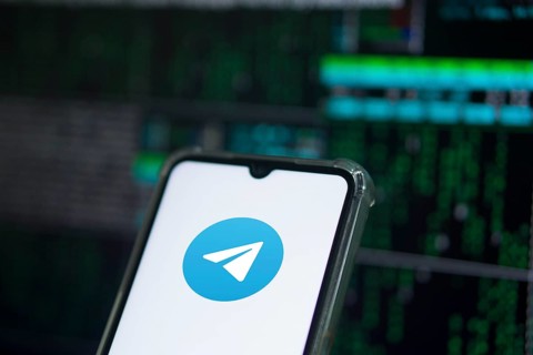 The TELEGRAM app logo on the screen of a cell phone that a man is holding.