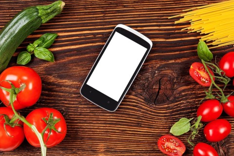 Fresh vegetables and pasta on wooden table with smartphone and recipe on screen. Groceries, recipe