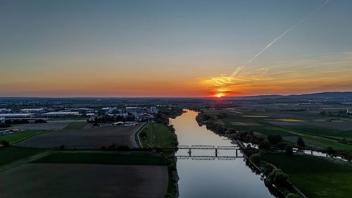 Wide river landscape with railway bridge in the middle, setting sunlight and extensive fields,