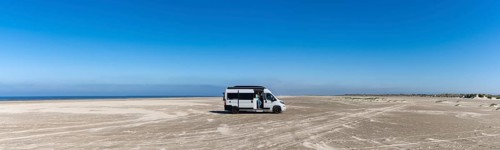 Ringby, Denmark: 31 May, 2021: panorama of a gray camper van parked on an endless white sand beach