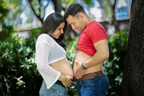 Pregnant couple holding their bellies in a park