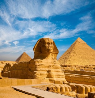Full profile of Great Sphinx including pyramids of Menkaure and Khafre in the background on a clear