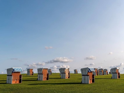 White beach chairs on a meadow and blue sky with clouds in the background, along the coast of the