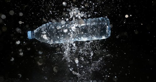 Bottle of Water falling on Water against Black Background