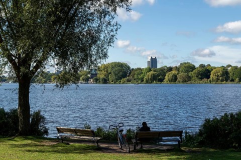 Leisure activities in summer, bicycle and woman on park bench, blue sky, Alster with Hotel