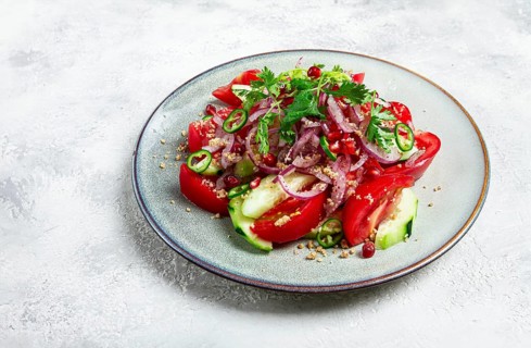 Georgian vegetable salad, cucumbers with tomatoes, greens, walnuts, pomegranate seeds, on a light