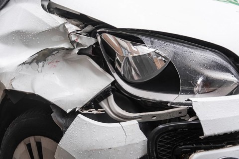 A heavily damaged white car after an accident. The front left mudguard is badly dented and