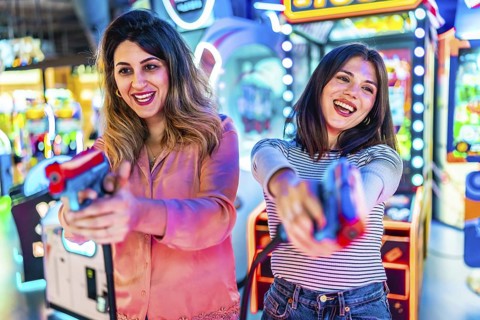 Two young women enjoying their free time playing together in an amusement arcade, holding toy guns