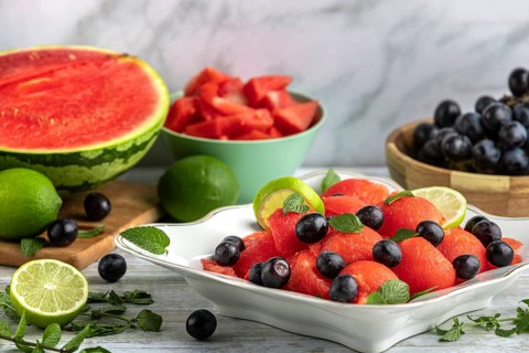 Bowl with sliced watermelon, grapes and limes in front of Ingredients