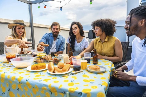 Cheerful friends sharing a meal together at a rooftop barbecue, enjoying grilled food, drinks, and