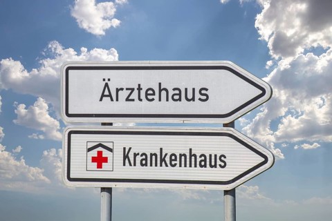 (Photomontage) Directional arrows with the inscription ÄRZTEHAUS and KRANKENHAUS against a blue sky