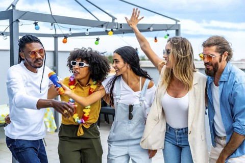 Group of diverse friends celebrating on a rooftop, singing karaoke, dancing joyfully, and enjoying
