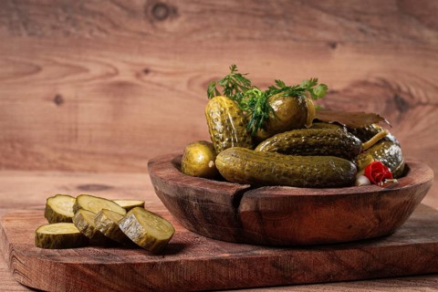 Pickled cucumbers in a wooden bowl with herbs and spices, close-up, rustic style