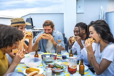 Cheerful multi ethnic friends savoring delicious burgers while enjoying a lively rooftop barbecue