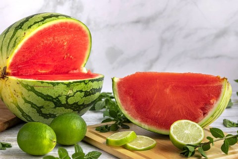 Sliced watermelon with limes and mint leaves on a wooden board
