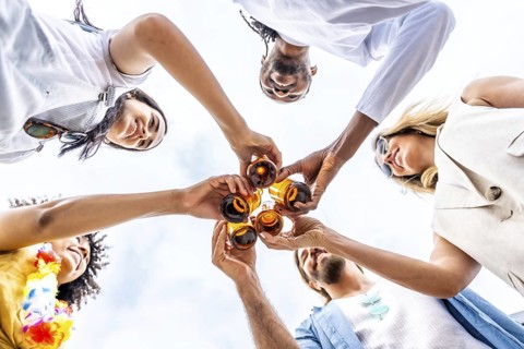 Group of cheerful multi ethnic friends toasting with beer bottles, enjoying a summer beach party