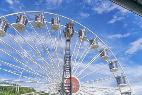 View of a high Ferris wheel with many baskets in front of a cloudy blue sky, fire brigade exercise