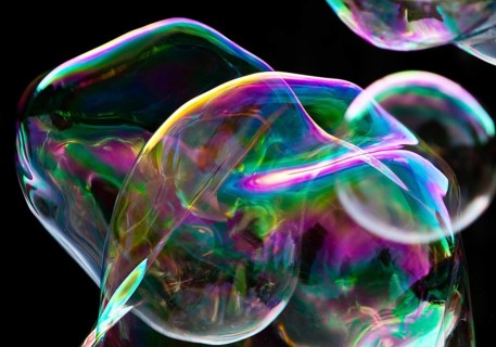 Large, irregular, iridescent soap bubbles in the colours of the rainbow against a black background,