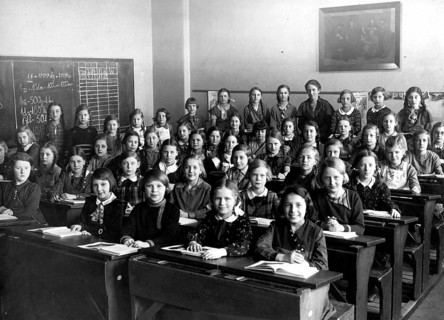Girls' class school bench, 1920s, A group of schoolgirls sitting on wooden benches in a classroom,