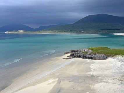 Dramatic sky over a calm beach with turquoise water and mountains in the background, Outer