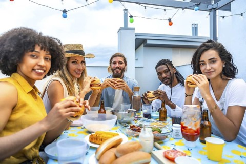 Cheerful multi ethnic friends savoring delicious burgers while enjoying a vibrant rooftop barbecue