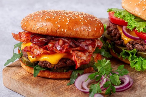 Two burgers with beef patty, fried bacon, cheddar cheese, tomatoes, homemade, no people