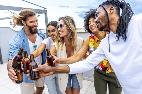 Happy friends celebrating on a rooftop, toasting with beer bottles and enjoying quality time