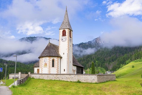 Church with tower and clock, surrounded by meadows and mountains in an alpine landscape, Dolomites,