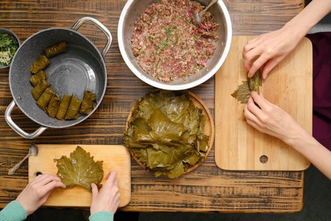 Overhead view of hands making dolma using vine leaves and a ground meat on a kitchen table