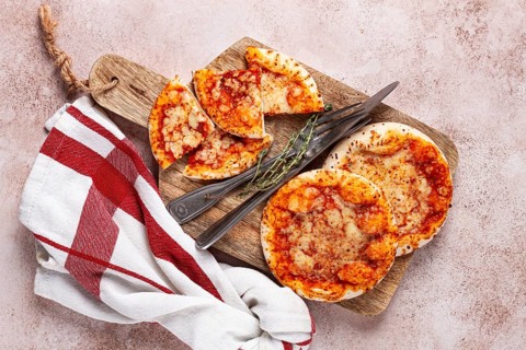 Four pizzetta Margaritas, on a cutting board, on a light gray surface, top view