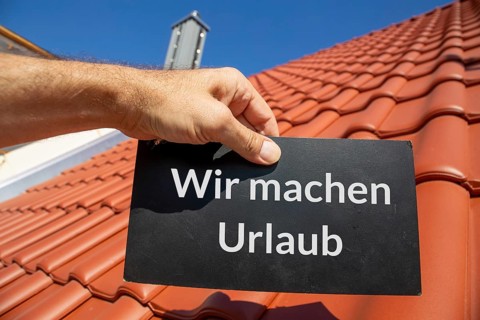 Roofer on holiday: Man holding a sign (with added text) WIR MACHEN URLAUB in front of a new tiled