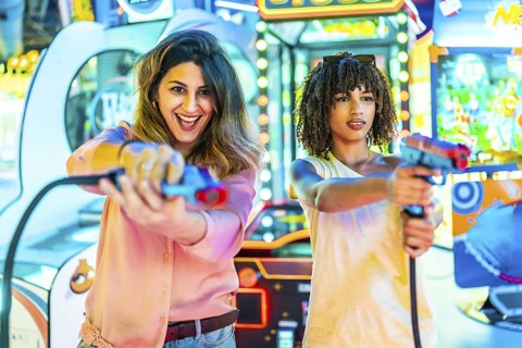 Two women enjoying their free time playing in an arcade with toy guns, laughing and having fun