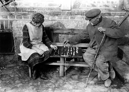 Old man playing chess with girl 1900, Two elderly people playing chess on a bench outdoors,