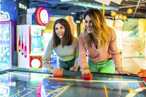 Two young women enjoying a friendly game of air hockey in a vibrant arcade, showcasing fun and